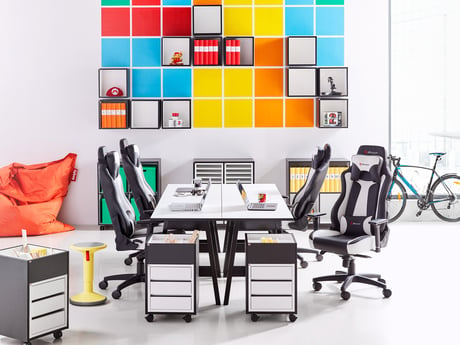 Biuro na otwartym planie z czarnymi szufladami biurka, czarnymi krzesłami biurowymi i 4 biurkami połączonymi razem, tworząc duży stół.
