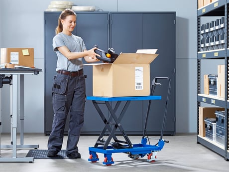 A woman standing by a lifting trolley unpacking products from a box