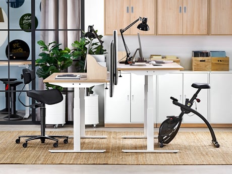 Dva elektropodizna stola sa stolicom sedlom i stolnim biciklom za vježbanje.