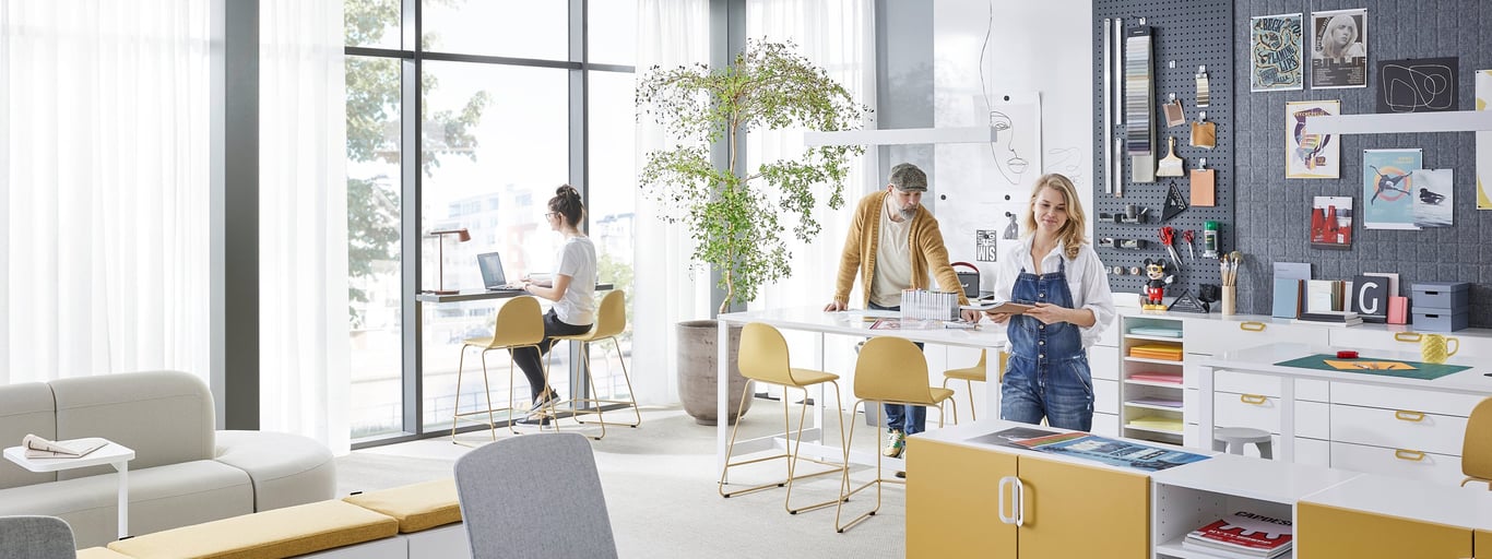 Terviklikult sisustatud kontoriruum, kus töötavad kolm inimest - fookuses QBUS hoiumööbel