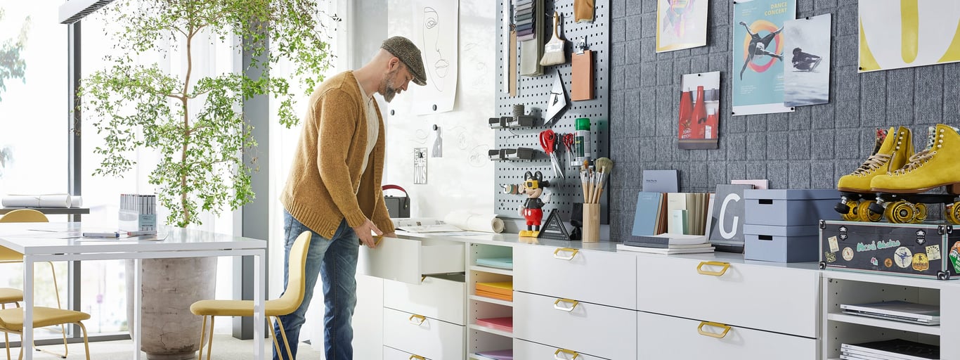 Man standing up and reaching into a storage drawer unit in an office