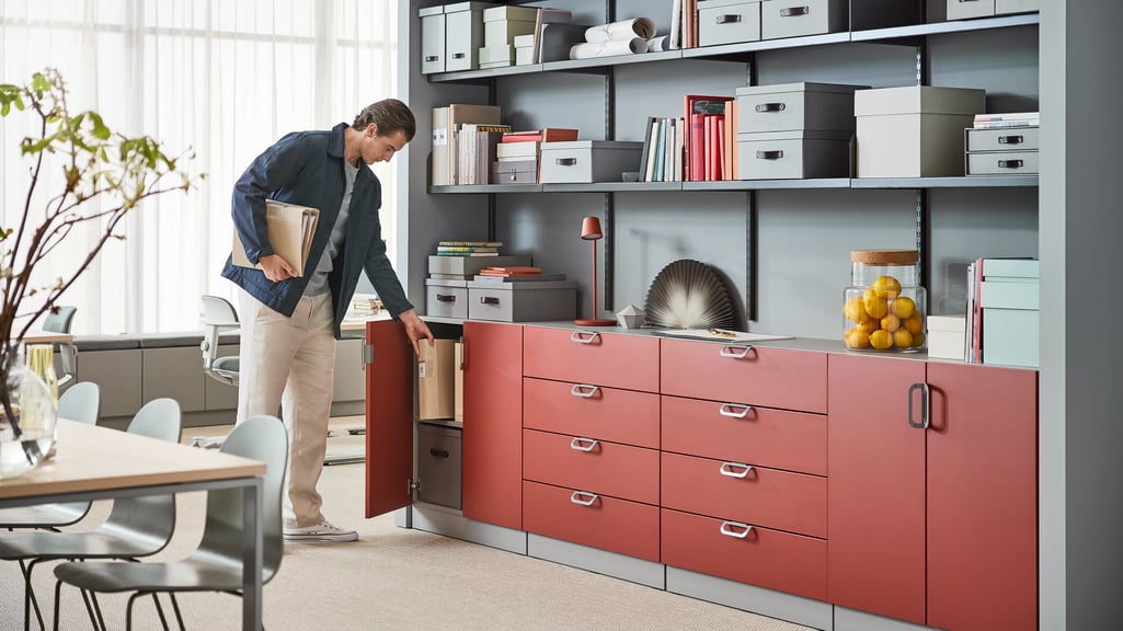 A man stands to access a cabinet on a wall of red storage cabinets in an office.