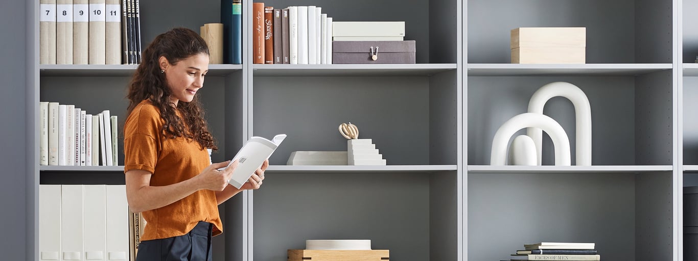 Woman stands in front of some storage cabinets and reads a book