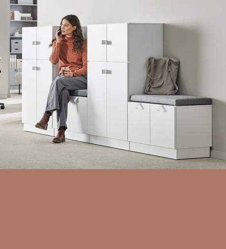 Moteris kalbasi telefonu sėdėdama ant biuro spintelės