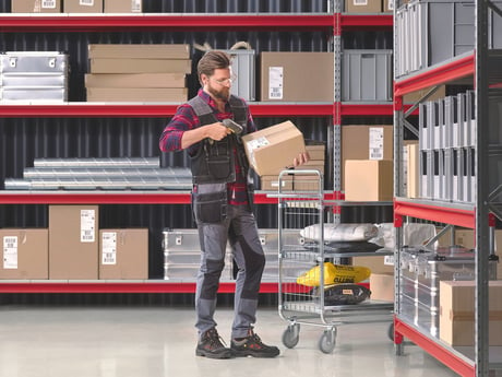 A person standing in a warehouse holding a package next to warehouse shelves