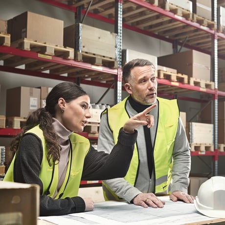 Two people standing looking at design plans in a warehouse