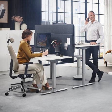 Two people at their office desks with one standing and the other sitting
