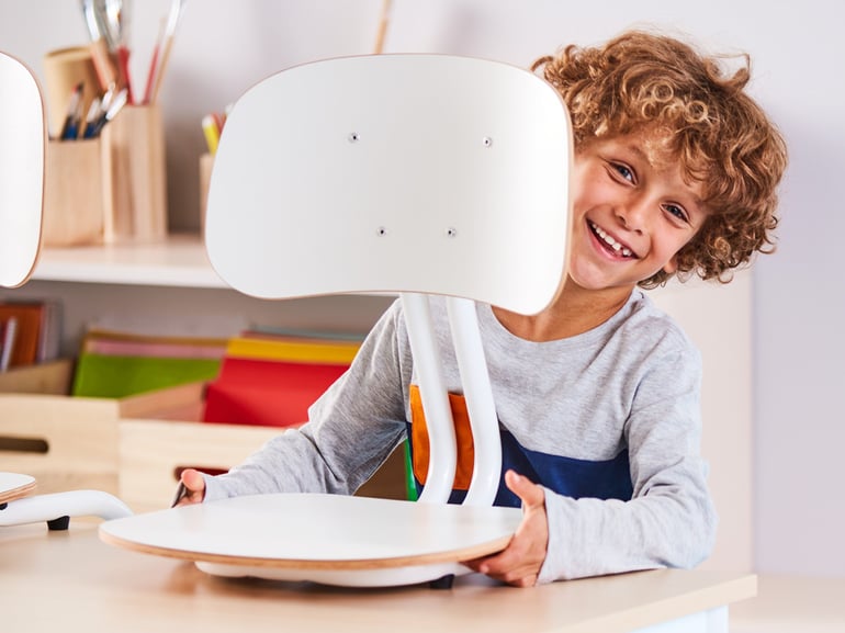 Laps seisab lauale riputatud YNGVE õpilastooli taga ning naeratab kaamerasse