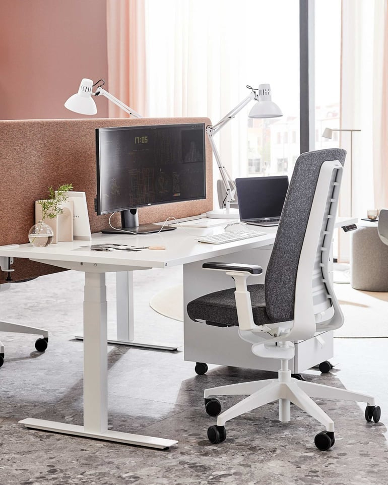 En skrivebordsplads med hæve sænkebord, kontorstol og bordskærme